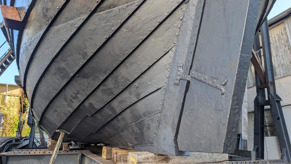 Traditioneller Holzbootsbau und Plankenwechsel am Rumpf einer historischen Hansekogge auf der Rathje Werft