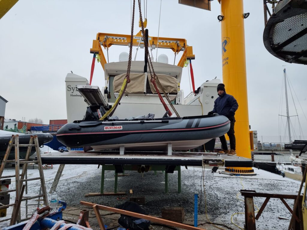 Ein Kran hebt das Suzumar Schlauchboot zur Passprobe auf die neuen, maßgefertigten Keile auf der Badeplattform.